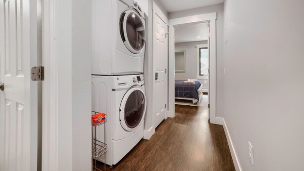 Una lavanderia con lavatrici e asciugatrici affiancate, un letto nella camera comunicante e un corridoio che porta al bagno.