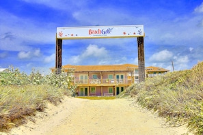 A beachfront hotel with a prominent BeachGate sign, multiple balconies, and a sandy pathway leading to the entrance. - Beachgate Condo Suites And Hotel 532a+532b 2 Bedroom Condo (Port Aransas)