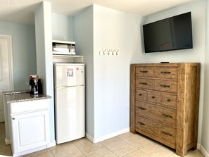 A compact kitchen with a refrigerator, a coffee maker, a wooden cabinet, and a mounted television. - Beachgate Condo Suites And Hotel 532a+532b 2 Bedroom Condo (Port Aransas)