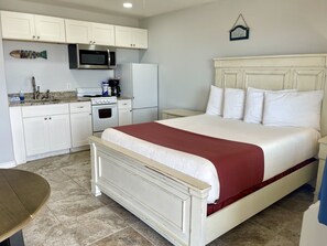 A bedroom with a bed, a nightstand, a dresser, a microwave, a refrigerator, and a sink in a kitchenette. - Beachgate Condo Suites And Hotel 225+226 2 Bedroom Condo (Port Aransas)