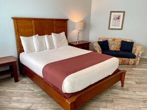 A large bed with a wooden headboard, a bedside table with a lamp, a patterned sofa, and a framed picture on the wall. - Beachgate Condo Suites And Hotel 517a+517b 2 Bedroom Condo (Port Aransas)
