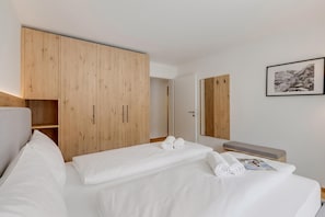 A hotel room with a bed, a wooden wardrobe, a mirror, and a framed picture on the wall. - Residenza Castanea 104 San Bernardino Alpine Apartments, San Bernardino, Switzerland (San Bernardino)