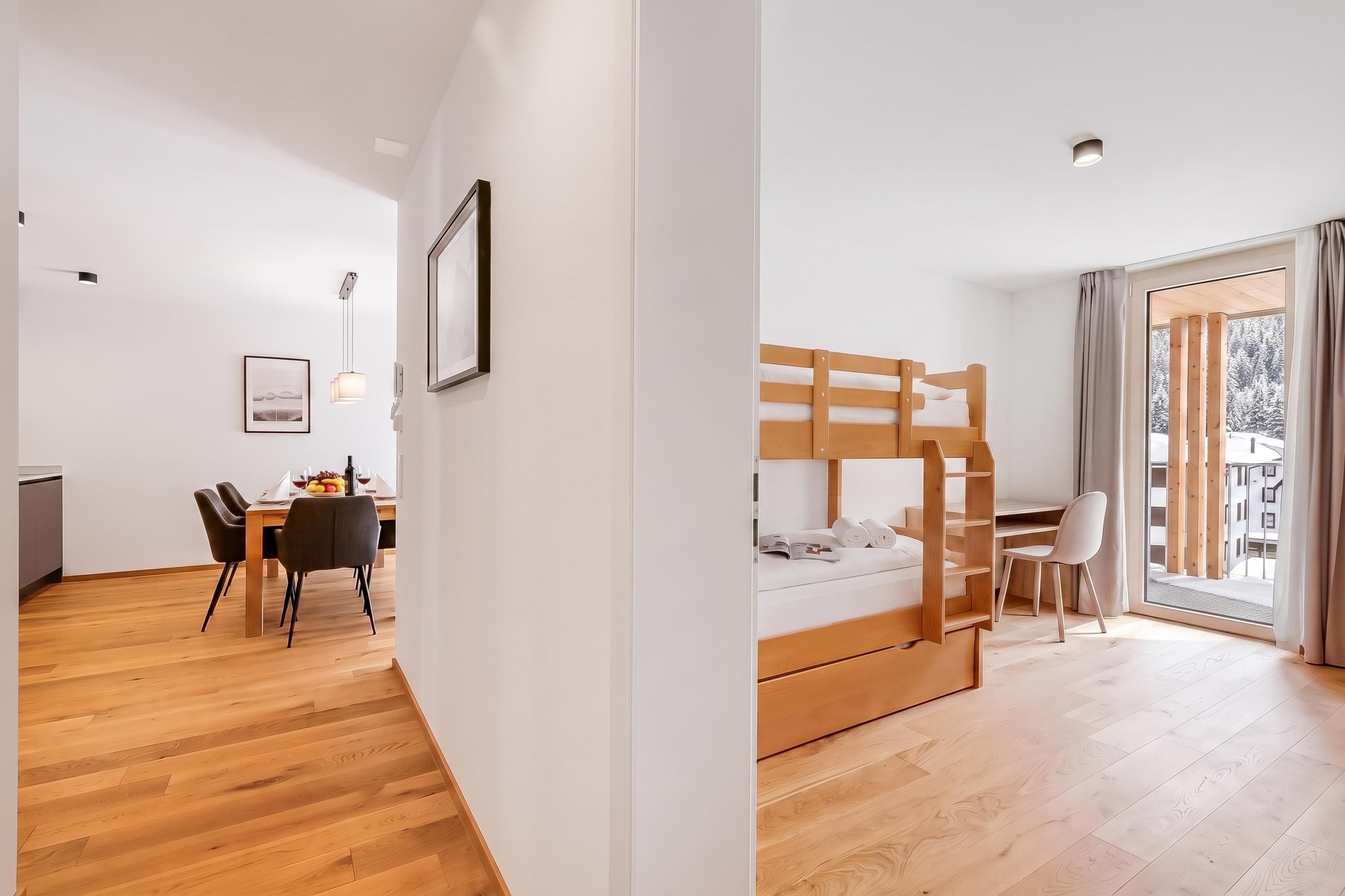 A modern hotel room with a wooden bunk bed, a dining area with a table and chairs, and a large window with a view.