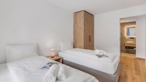 Et hotelværelse med to senge, en træskab, et natbord med lampe og et badeværelse, der kan ses gennem en åben dør.