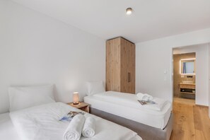Een hotelkamer met twee bedden, een houten garderobe, een nachtkastje met een lamp en een badkamer die door een geopende deur zichtbaar is.