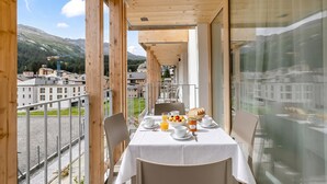 En balkon med et bord dækket til morgenmad, med udsigt over et bjergrigt landskab.