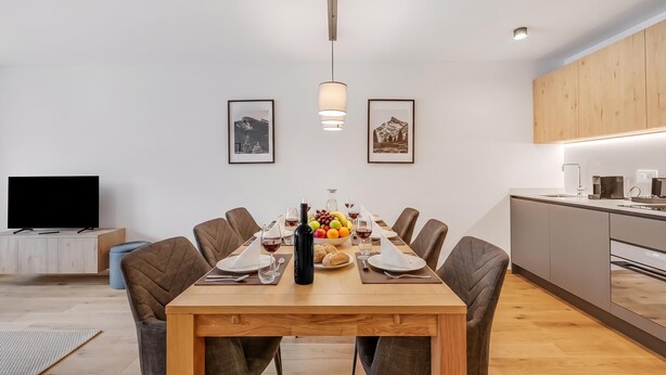 Et moderne spiseområde med et træbord, stole og et fjernsyn i baggrunden.