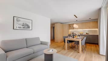 A modern living room with a grey sofa, a small round coffee table, and a dining area with a wooden table and chairs.