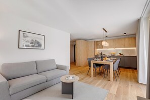 A modern living room with a grey sofa, a small round coffee table, and a dining area with a wooden table and chairs.
