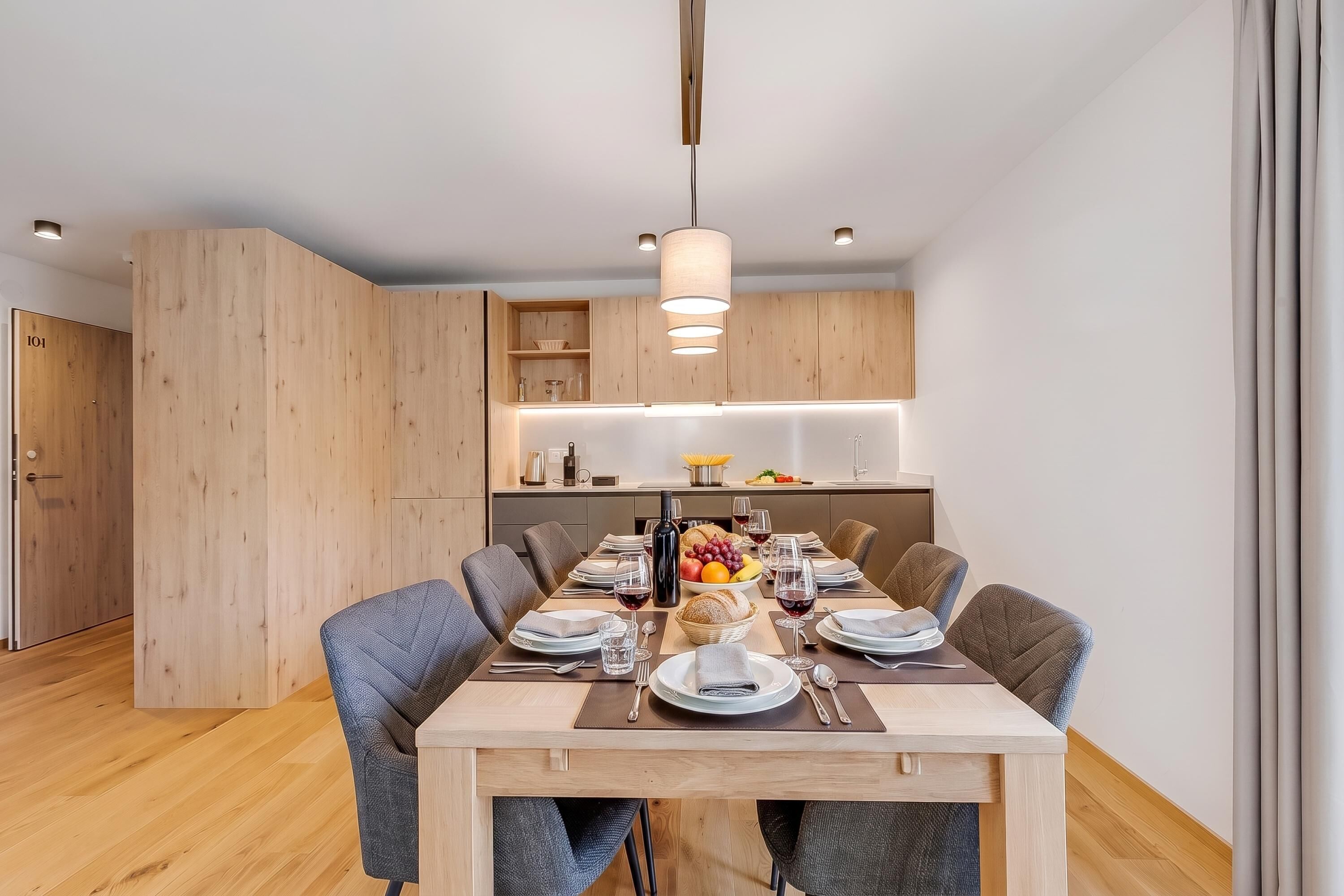 A modern dining area with a wooden table set for six, surrounded by chairs.