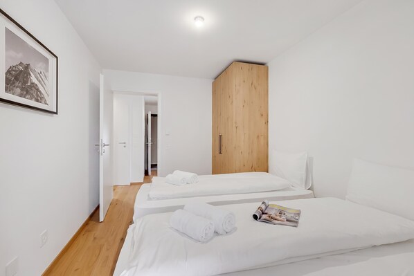 A modern hotel room with two beds, a wooden wardrobe, and a framed picture on the wall.