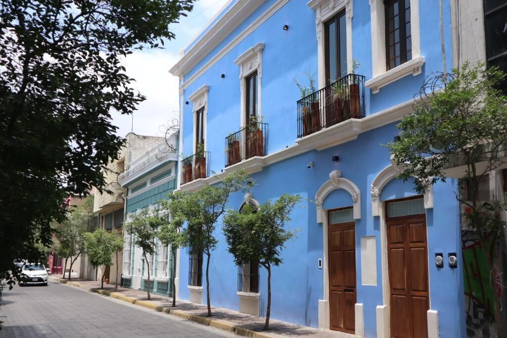 Una calle con edificios, incluyendo un edificio azul con balcones y una acera arbolada.