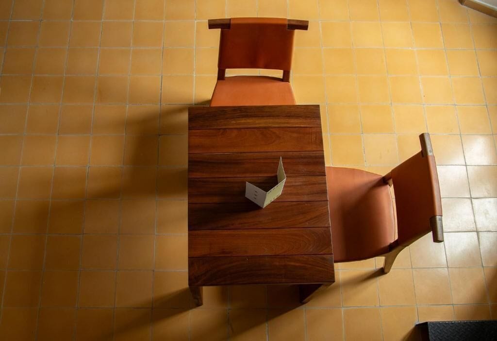 Una mesa de madera con una silla, una cómoda pequeña y un suelo de baldosas.