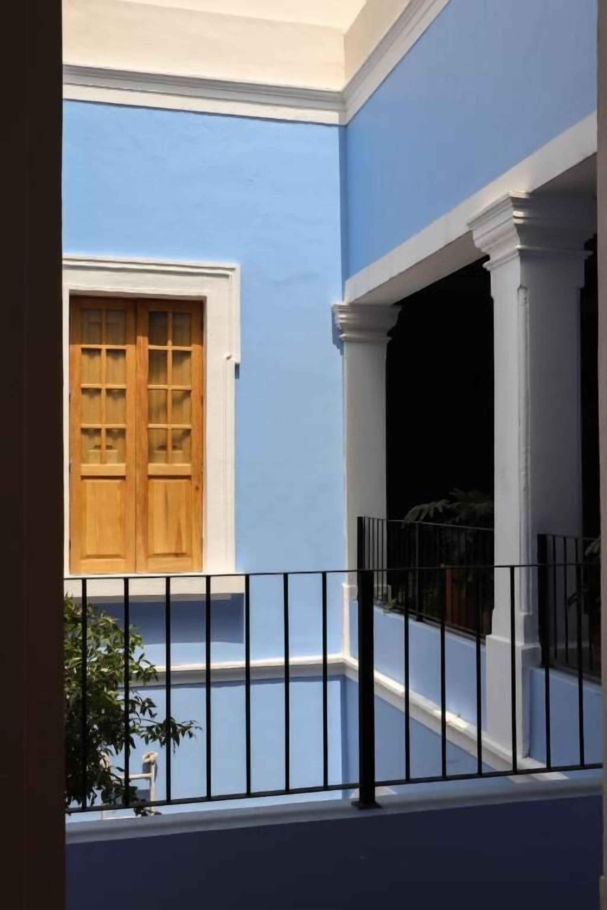 Pared exterior azul con una puerta de madera y una cerca de metal negro.