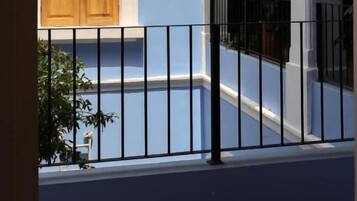 Pared exterior azul con una puerta de madera y una cerca de metal negro.
