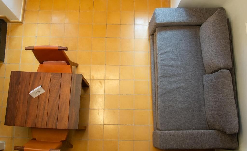 Una habitación con un armario de madera, un sofá gris y suelo de baldosas.