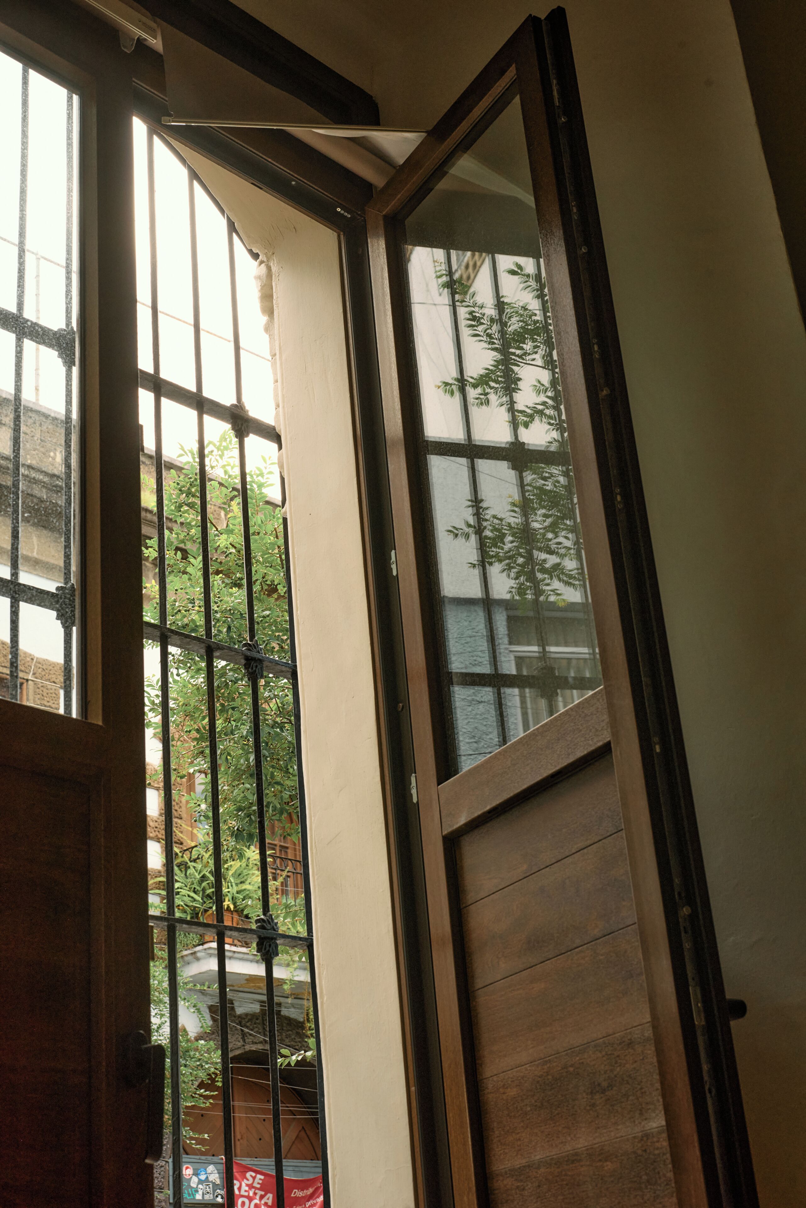 A room with a sliding door leading to a balcony, a window with metal bars, and a view of greenery outside.