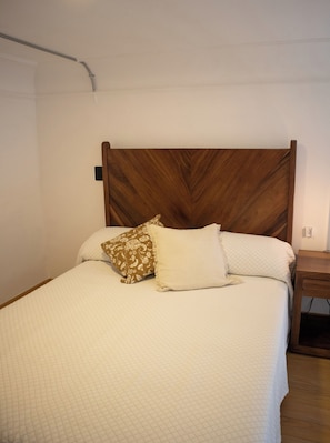 A bed with a wooden headboard, two pillows, and a bedside table with a lamp. - Lopez Cotilla 658 (Guadalajara)