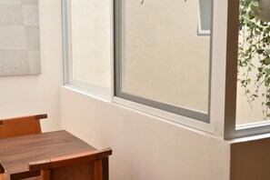 A room with a wooden table and chairs, a window with a view of greenery outside, and a wall with a textured pattern. - Lopez Cotilla 658 (Guadalajara)