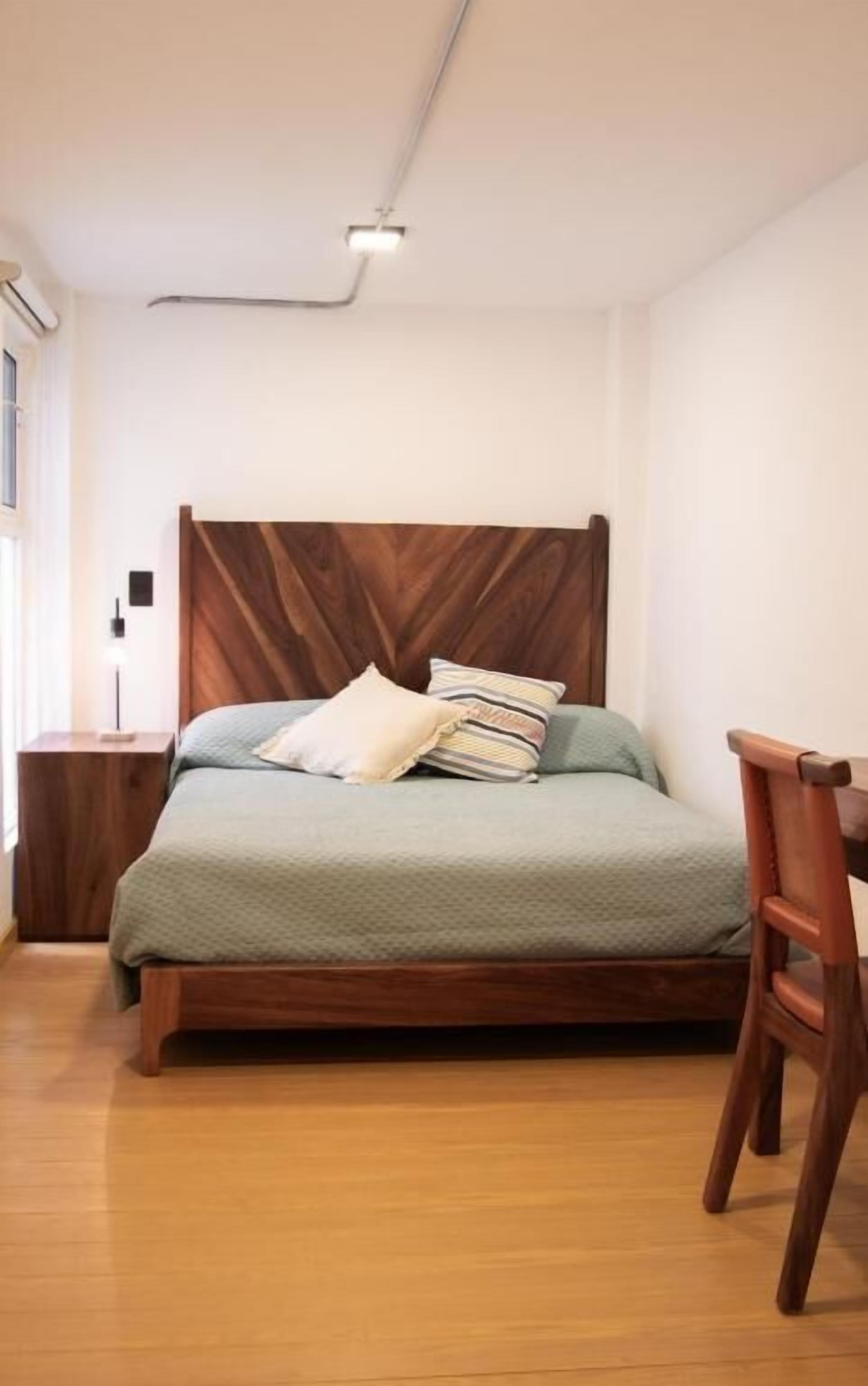 Un dormitorio con estructura de cama de madera, colcha verde y mesita de noche de madera.