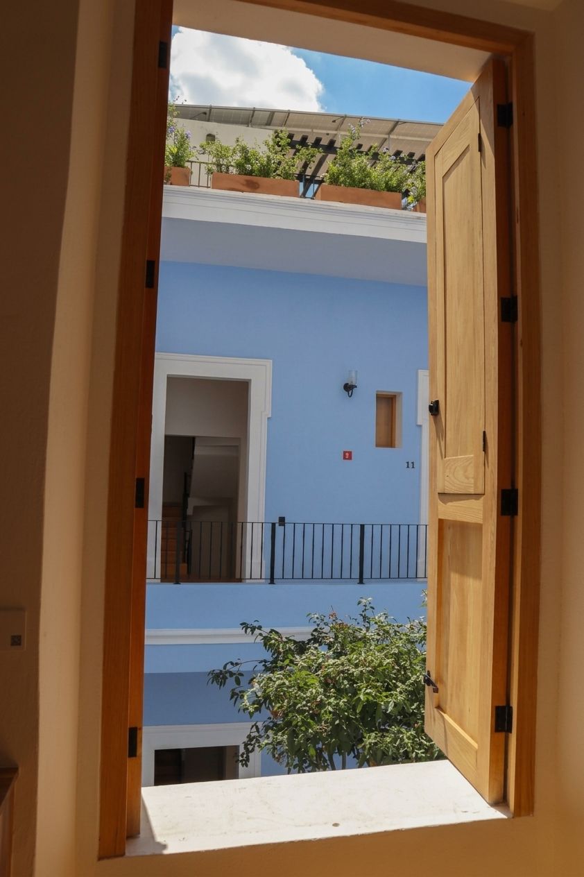 An open wooden door leading to a balcony with a view of a blue building and a tree.