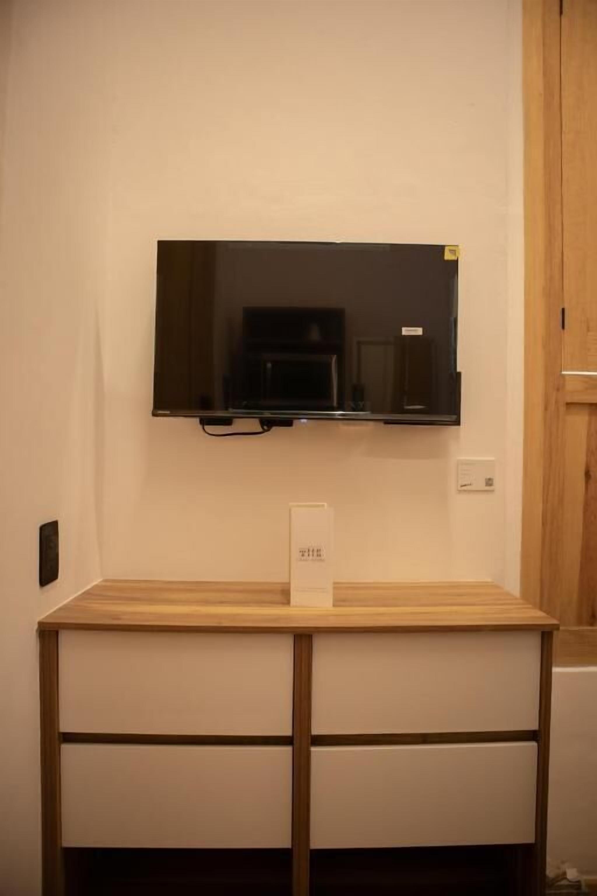 A flat-screen TV mounted on a wall above a wooden table with drawers.