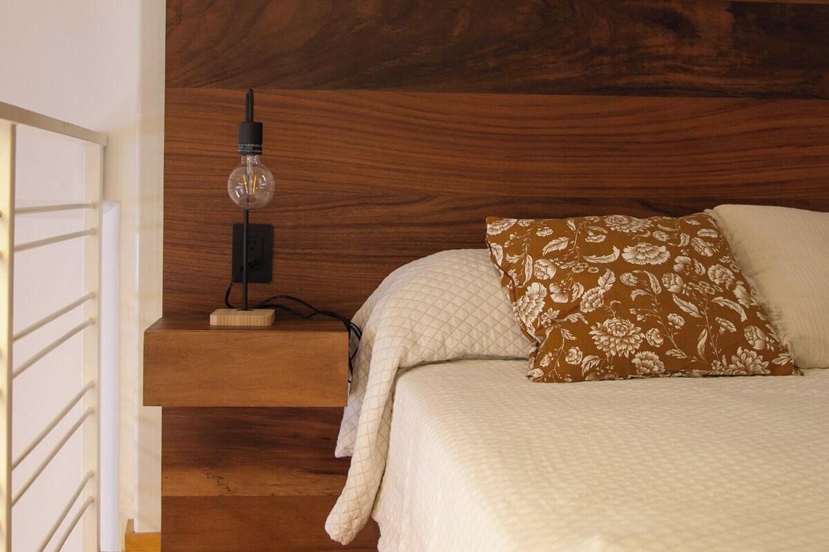 A bedroom with a wooden headboard, a bedside lamp, a floral pillow, and a quilted bedspread.
