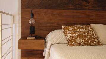 Un dormitorio con cabecera de madera, lámpara de noche, almohada estampada con flores y colcha acolchada.