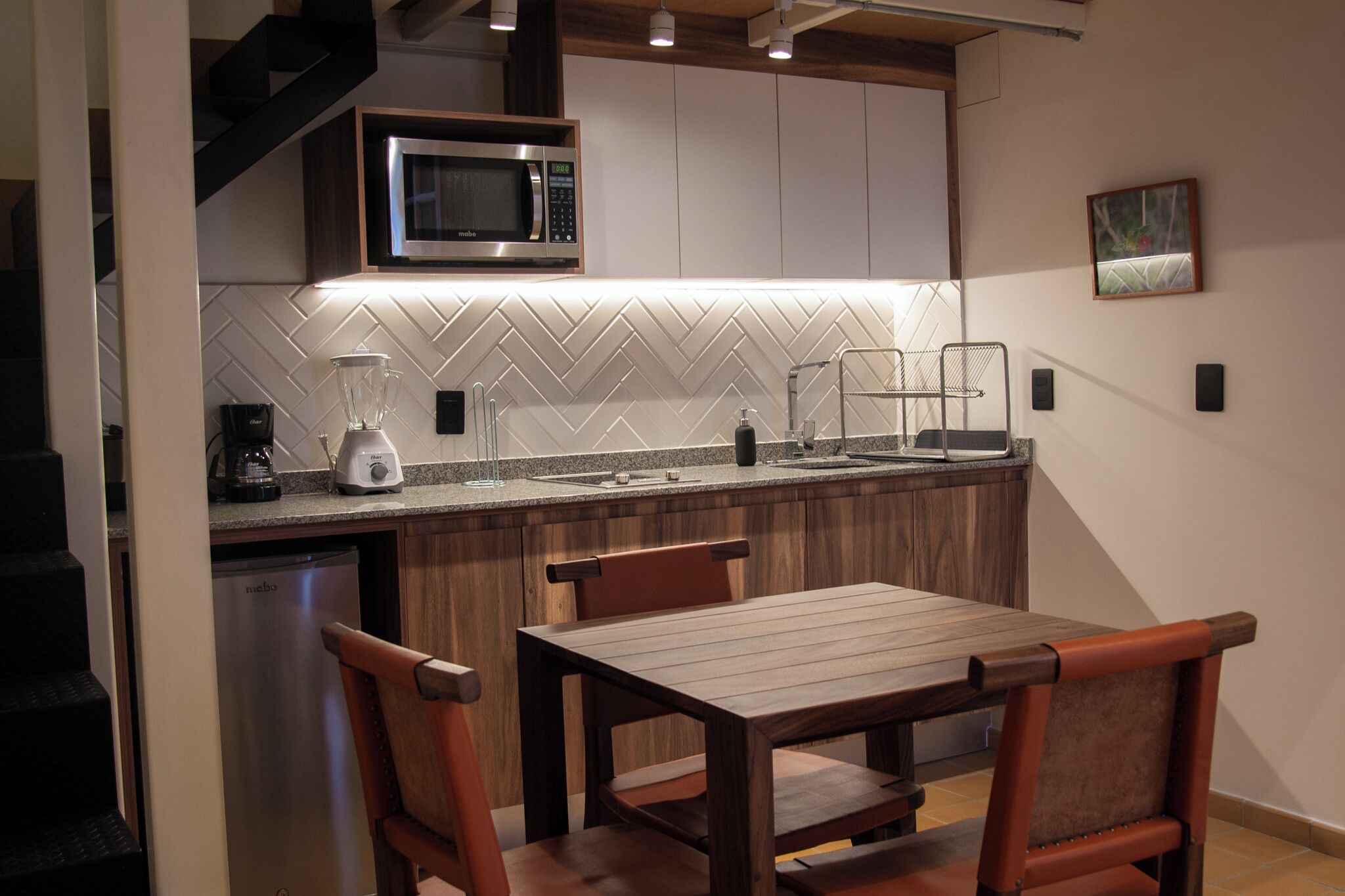 Una cocina compacta con microondas, licuadora y un salpicadero con diseño de espiga.