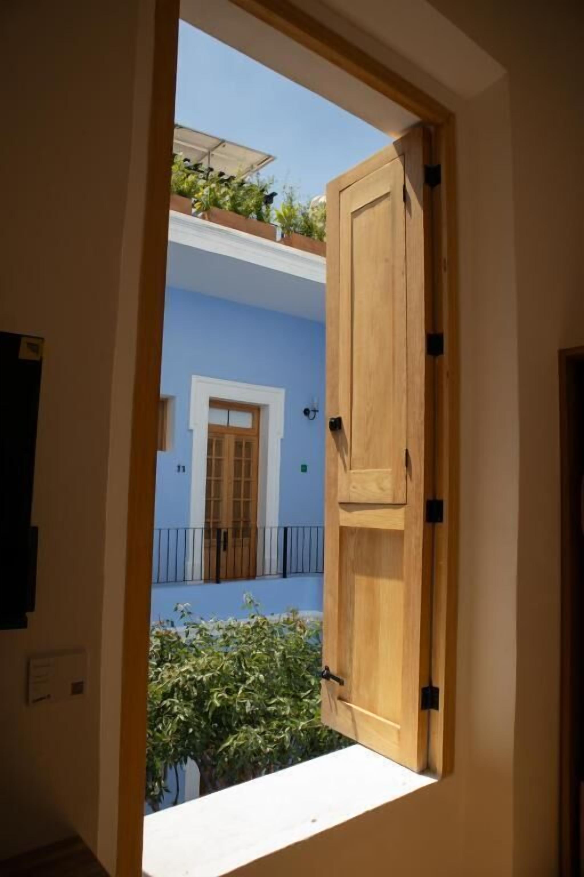 A wooden door leading to a balcony with a blue wall and a window.