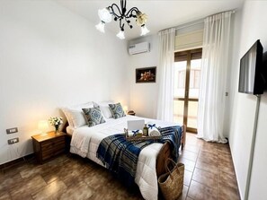 A bedroom with a bed, bedside table, lamp, air conditioning unit, window with curtains, and a television. - Gloria Apartment in Gallipoli (Gallipoli)
