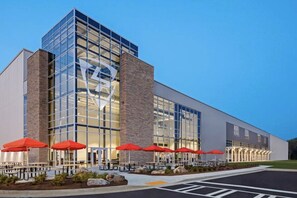 A modern building with a glass facade, outdoor seating with red umbrellas, and a clear sky.
