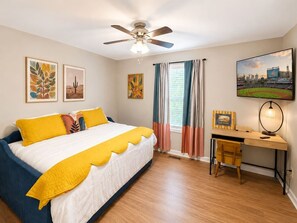 A bedroom with a bed, a desk, a chair, a ceiling fan, and a window with curtains. - Game Day Getaway | 5 Min to LakePoint | Sleeps 7 (Emerson)