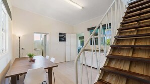 Un interior moderno con una escalera de madera, un comedor con mesa y sillas, y una cocina visible al fondo.
