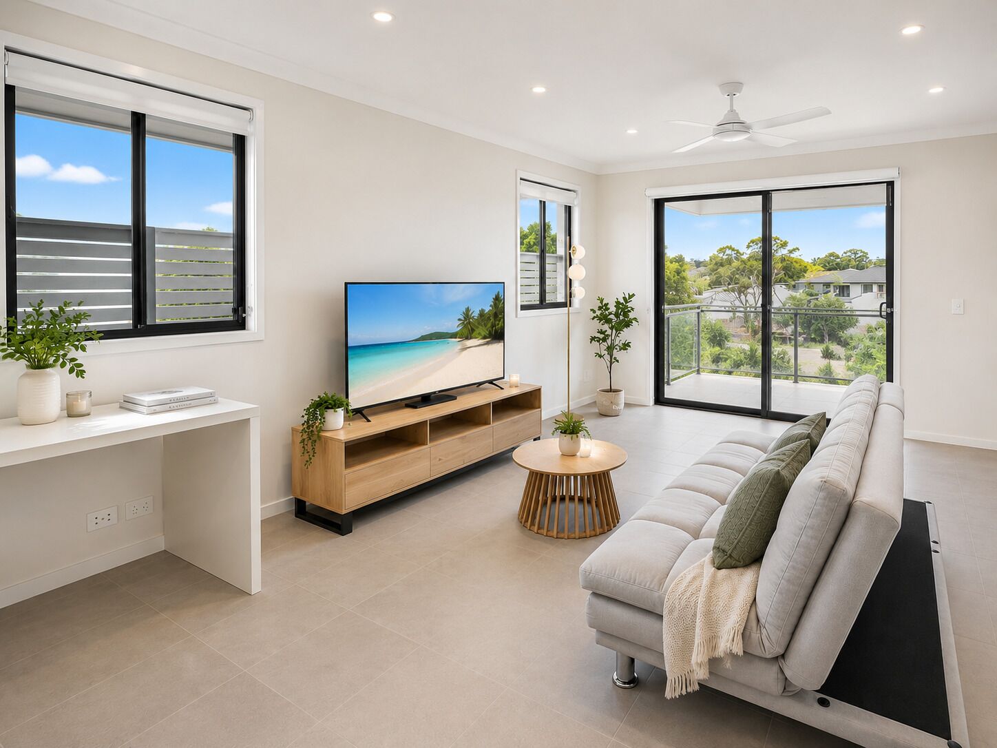 A modern living room with a flat-screen TV, a sofa, a coffee table, and a balcony with a view.