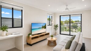 A modern living room with a flat-screen TV, a sofa, a coffee table, and a balcony with a view. - The Sunny Nook - 20 mins to BNE CBD (Coopers Plains)