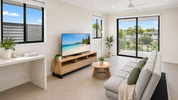 A modern living room with a flat-screen TV, a sofa, a coffee table, and a balcony with a view.