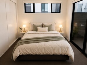 A bedroom with a bed, two bedside tables with lamps, a window, and a view of the outside.