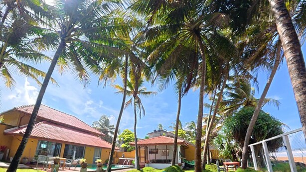 A tropical resort with palm trees, a pool, and outdoor seating. - Aura Beach Villa Deva 77 (Boossa)