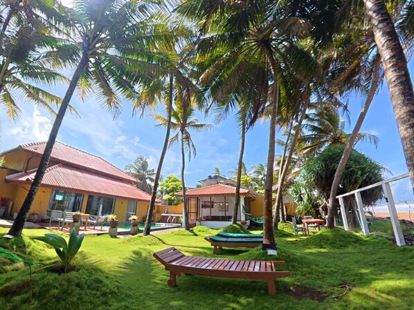 A tropical resort with palm trees, a pool, and outdoor seating.