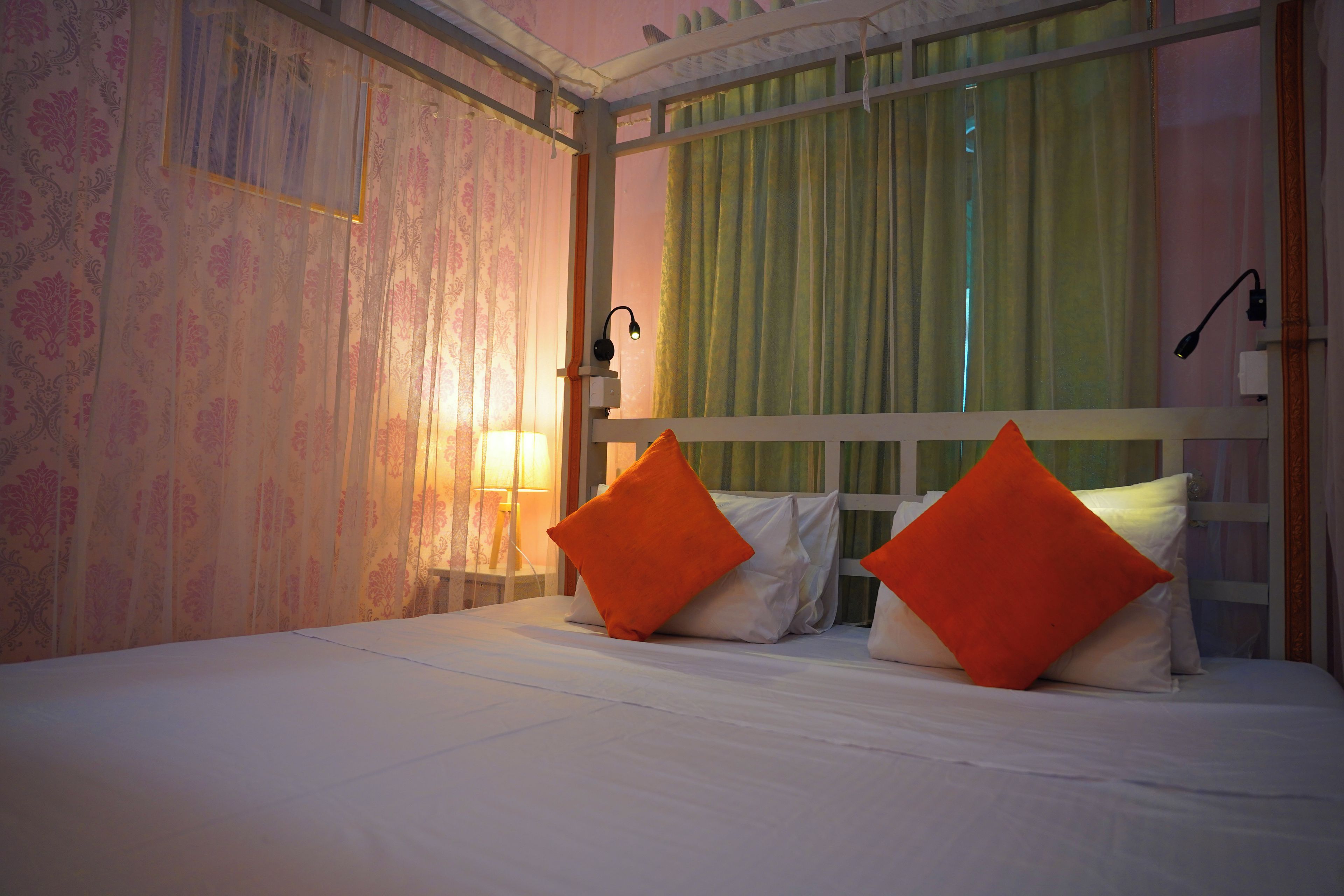 Habitación de hotel con cama, dos almohadas, mesita de noche, lámpara y ventana con cortinas.