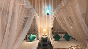 A room with two beds, each with a canopy and pillows, a bedside table with a lamp, and a patterned rug. - Aura Beach Villa Deva 77 (Boossa)