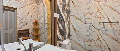 Un baño con un lavamanos grande de color blanco, un espejo y una pared de mármol.