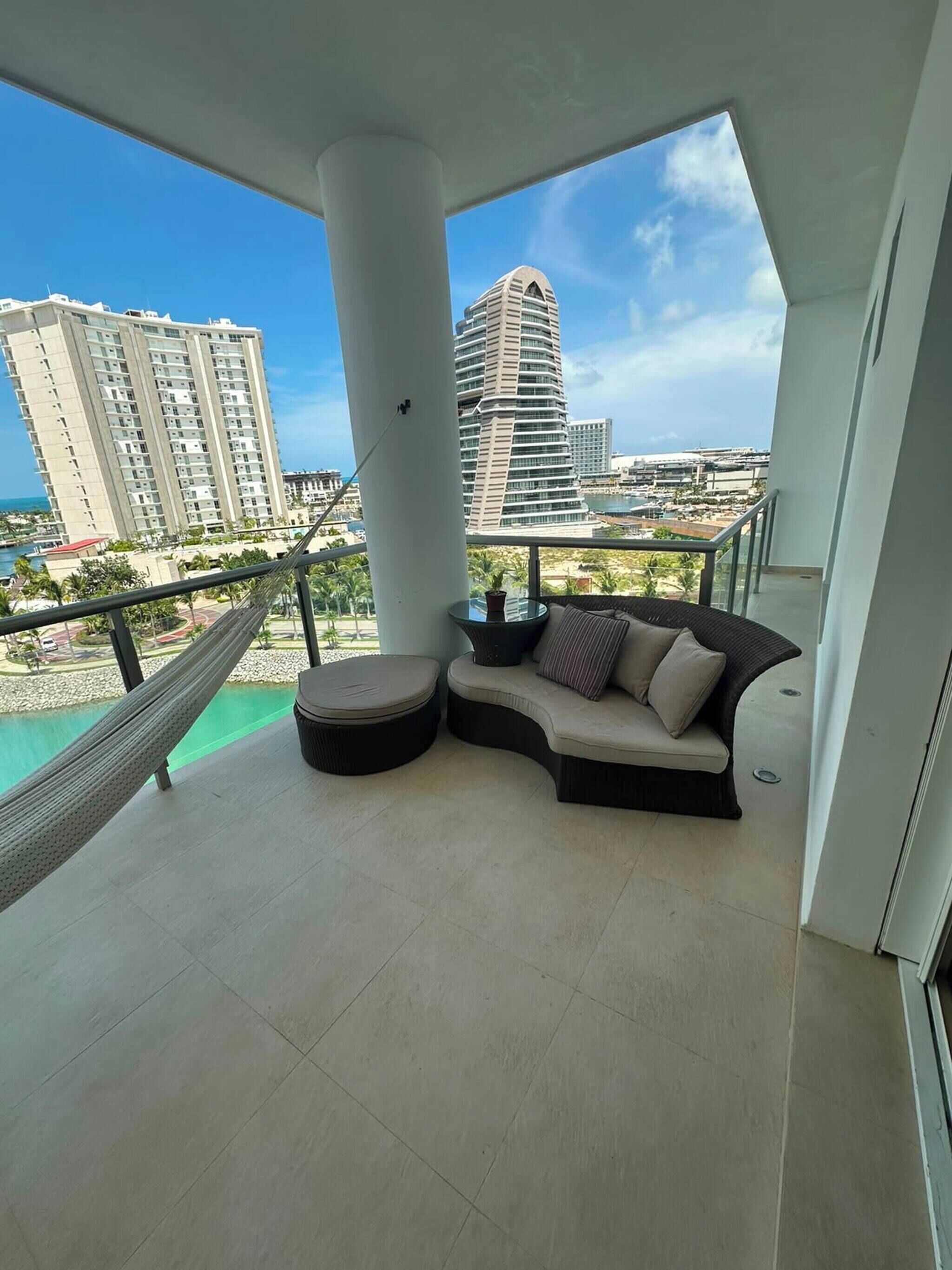 A balcony with a cushioned seating area, a hammock, and a view of a cityscape and water.