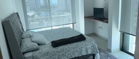 A bedroom with a bed, a television, a window with blinds, and a patterned rug.