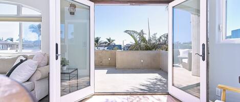 Puerta corrediza de vidrio abierta que da a un balcón con vistas a palmeras y edificios.