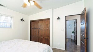Camera da letto con un letto grande, un armadio in legno, una ventola a soffitto e vista su un'altra stanza.