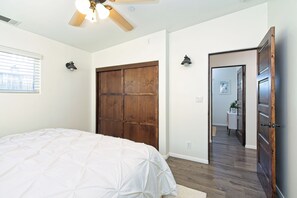 Ein Schlafzimmer mit einem großen Bett, einem Holzschrank, einem Deckenventilator und Blick in einen weiteren Raum.
