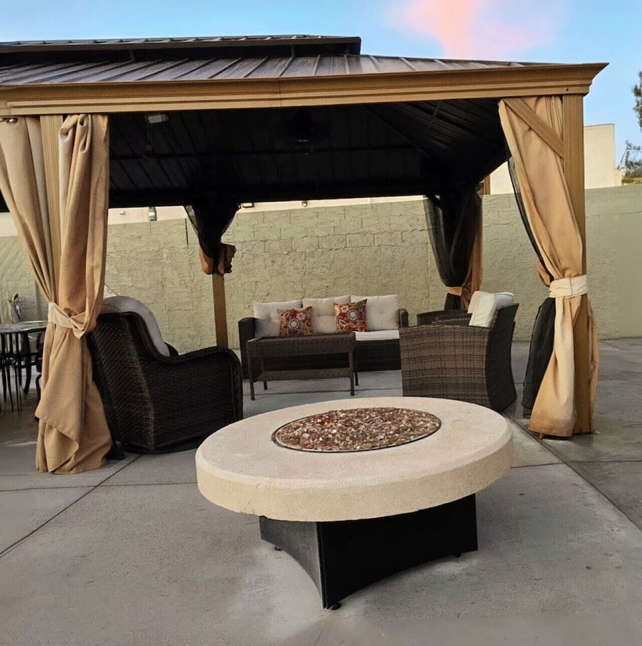 An outdoor patio with a round table, two chairs, a sofa, and a covered seating area with curtains.