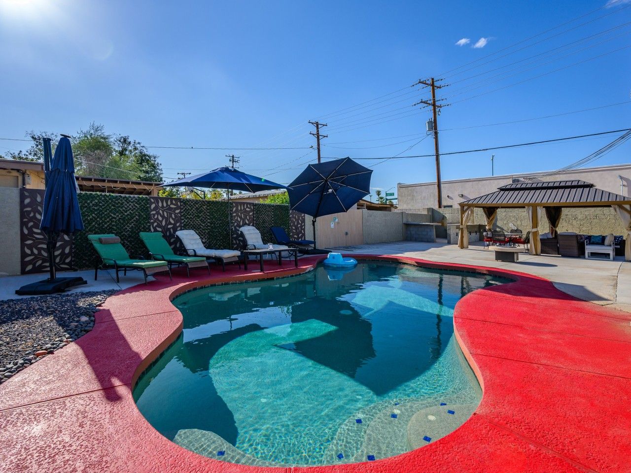A swimming pool with a red deck, lounge chairs, and umbrellas.